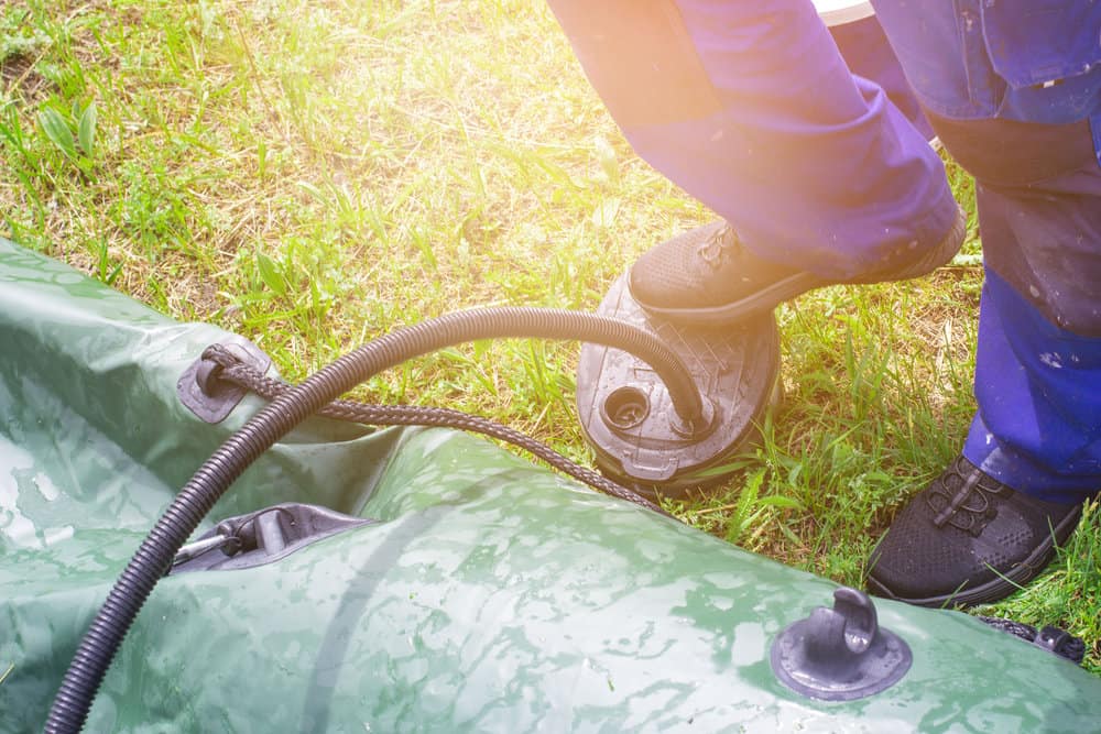 a man using foot pump to inflate a green inflatable boat