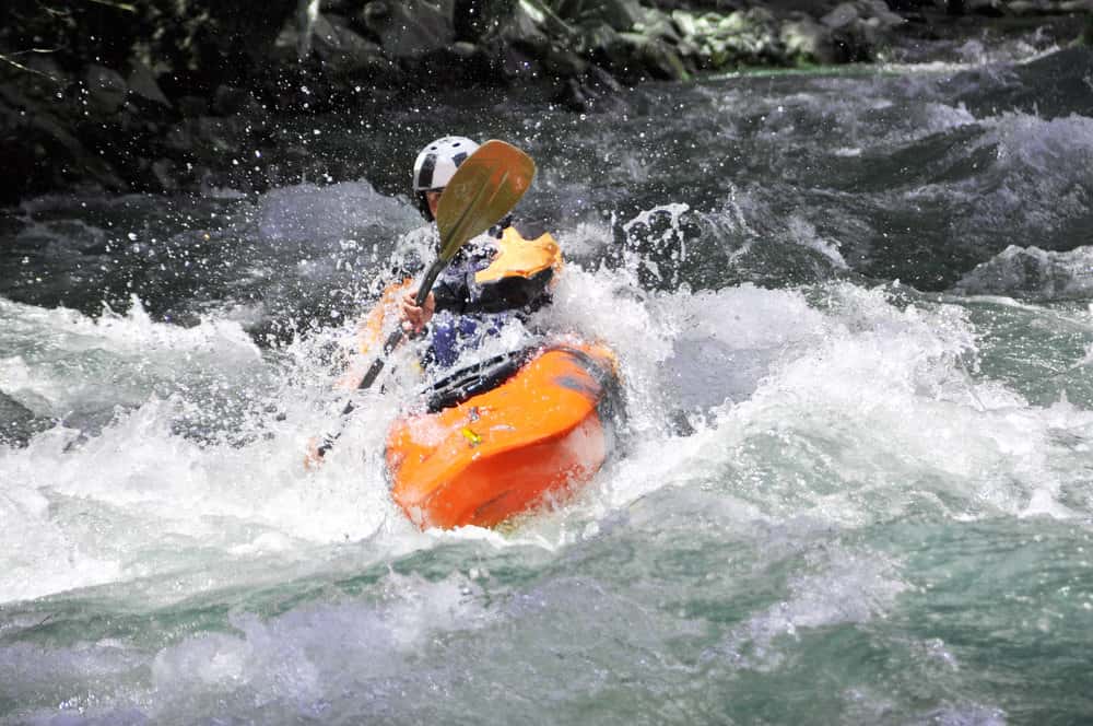 man kayaking with a short paddle in whitewater