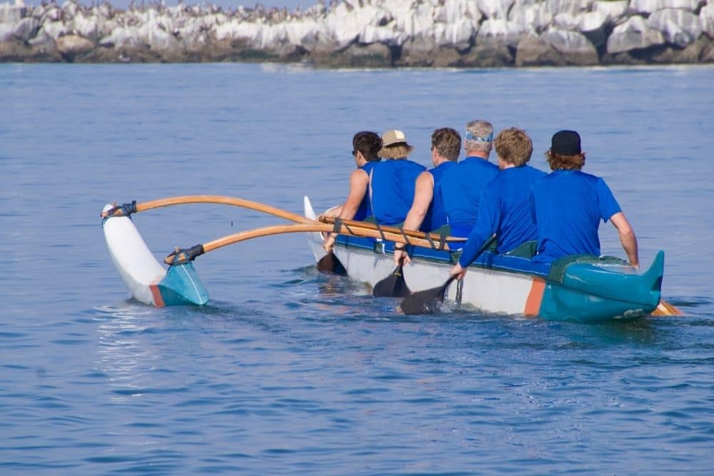a group of people trolling on a kayak with an outrigger