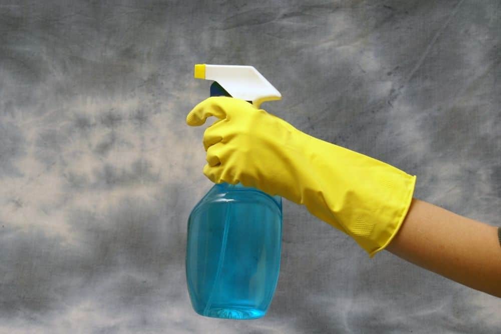 hand wearing yellow glove with a bottle spray containing mix of blue soap and water
