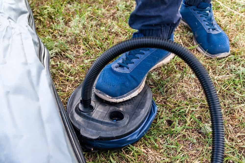 man using foot pump to fill a pontoon boat with air