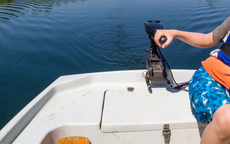 young boy driving a boat with an old electric trolling motor