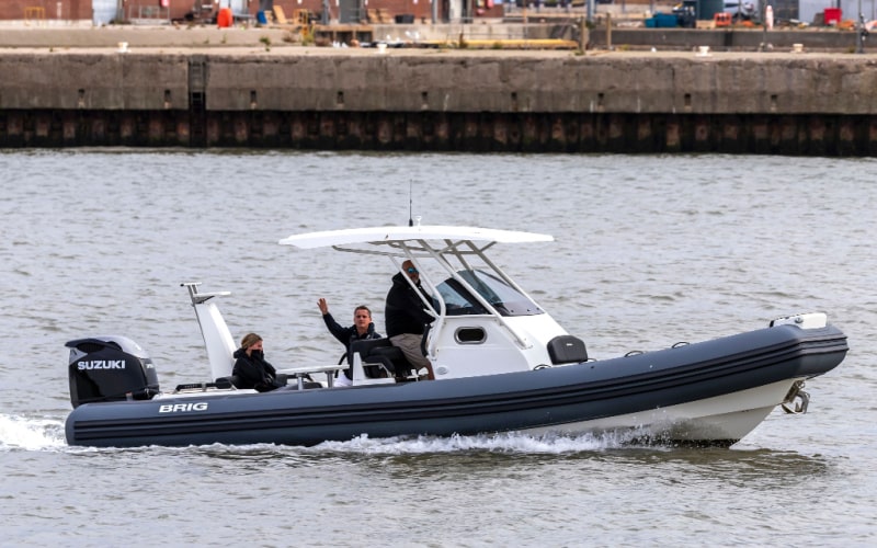 three people on a big Brig RIB equipped with an Suzuki outboard motor moving along a harbour