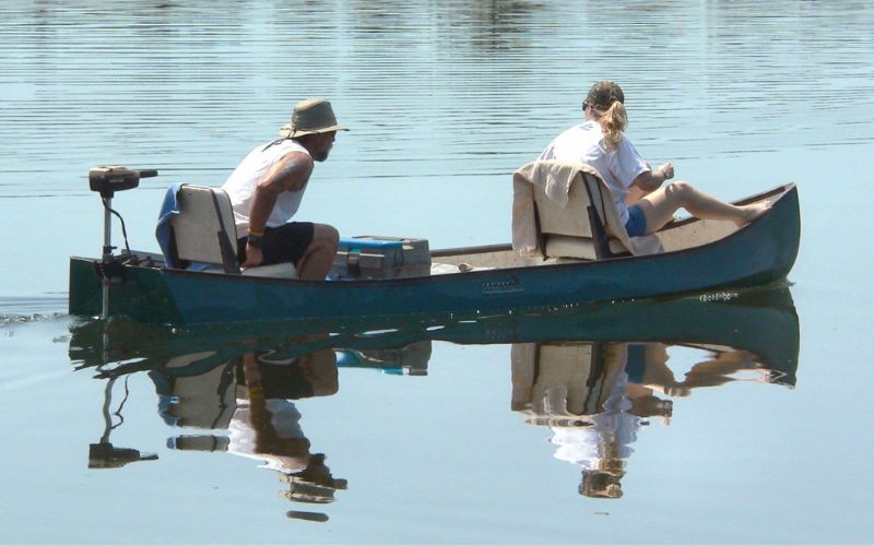 a couple is sitting on their canoe moving slowly through a calm water