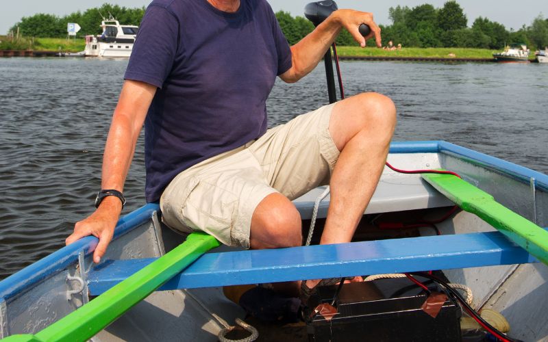 man sitting in his boat and controlling the trolling motor which is connected to a marine battery