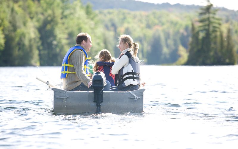 family enjoys their sunny day in a rowboat with outboard motor running on the water