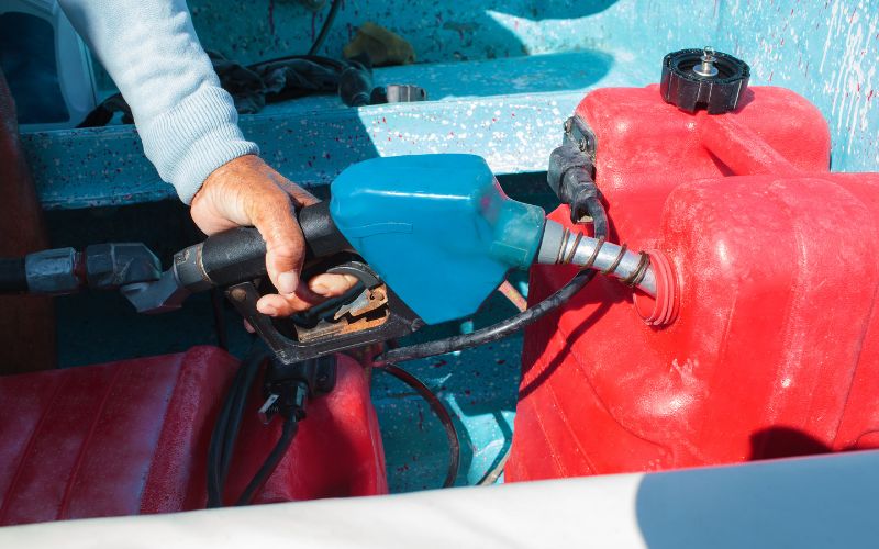 man is filling up the fuel tank of boat outboard motor