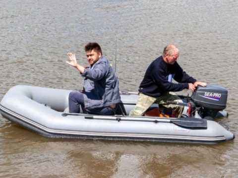 two fishermen are struggling with the outboard motor before sailing their inflatable boat