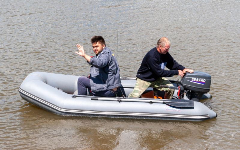 two fishermen are struggling with the outboard motor before sailing their inflatable boat