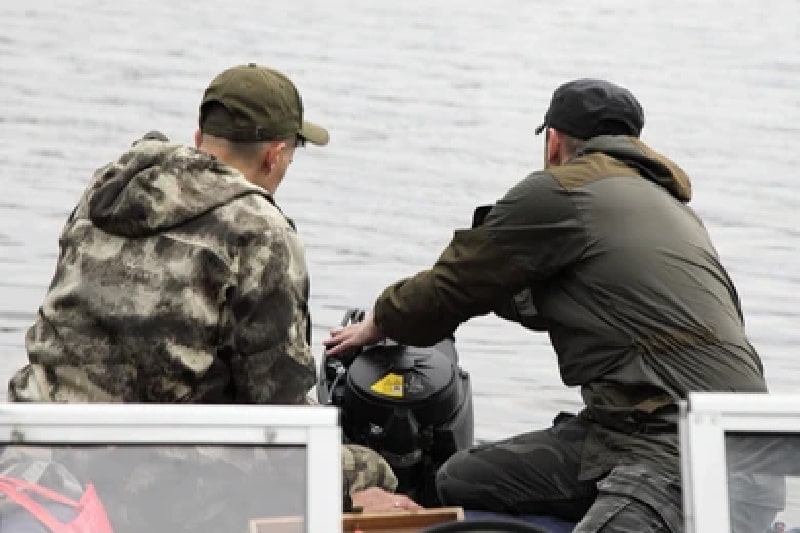 two men are fixing an broken outboard boat motor