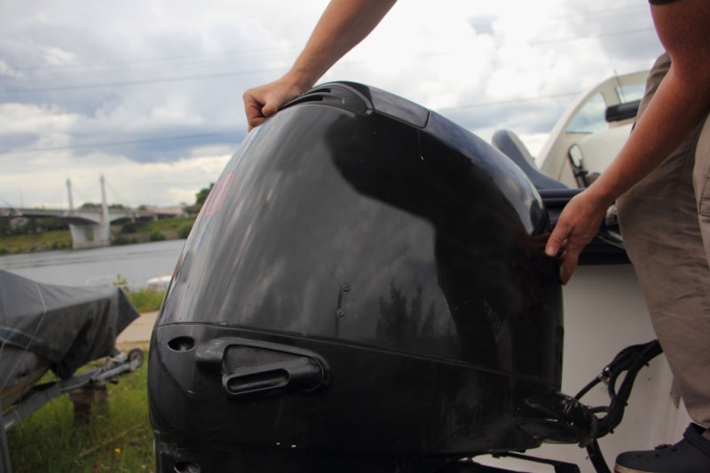 man removes the cover of an outboard motor on transom of boat