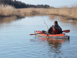 man is fishing in a small lake with his inflatable kayak